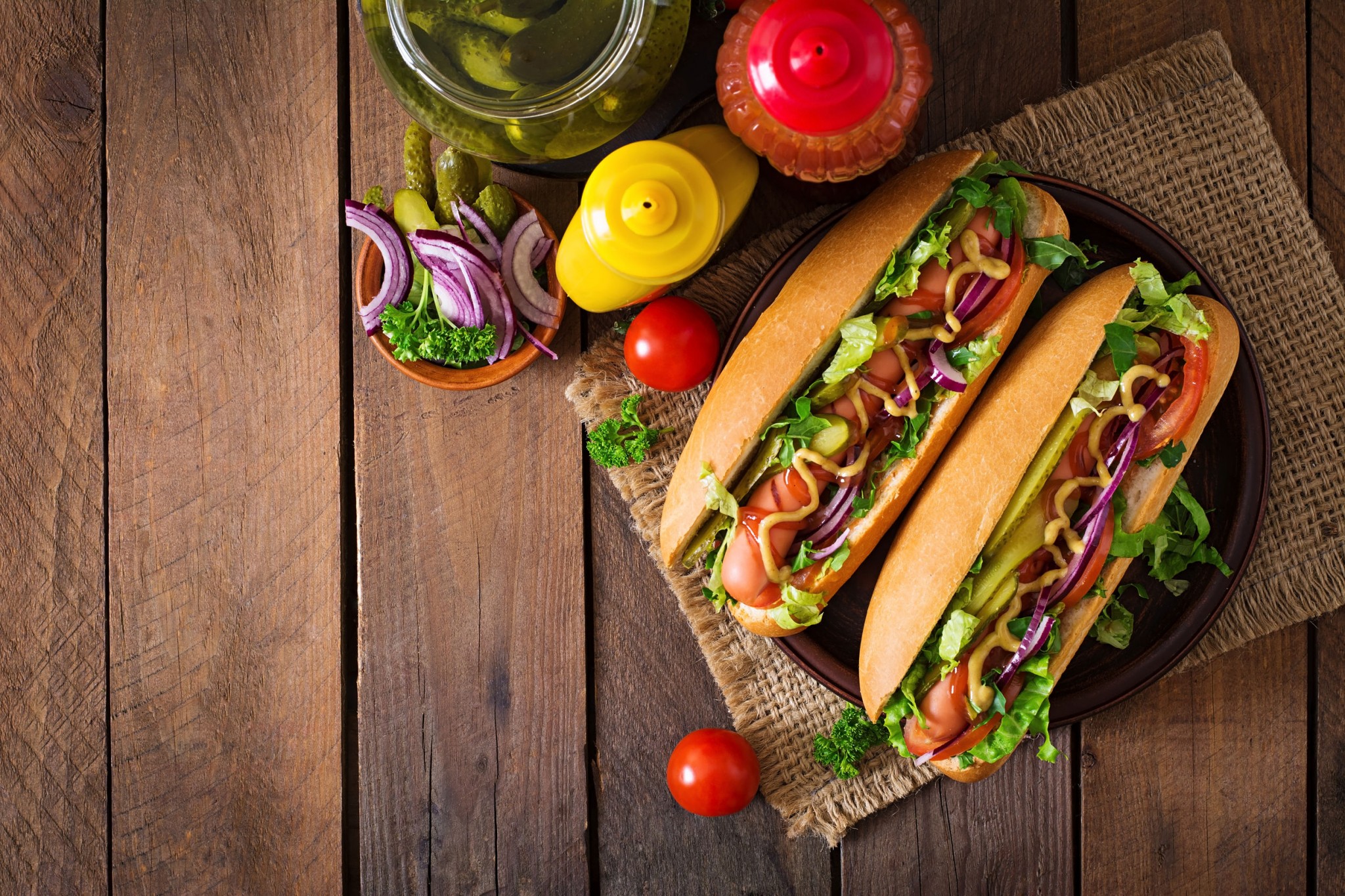 Hot dog with pickles, tomato and lettuce on wooden background. Top view